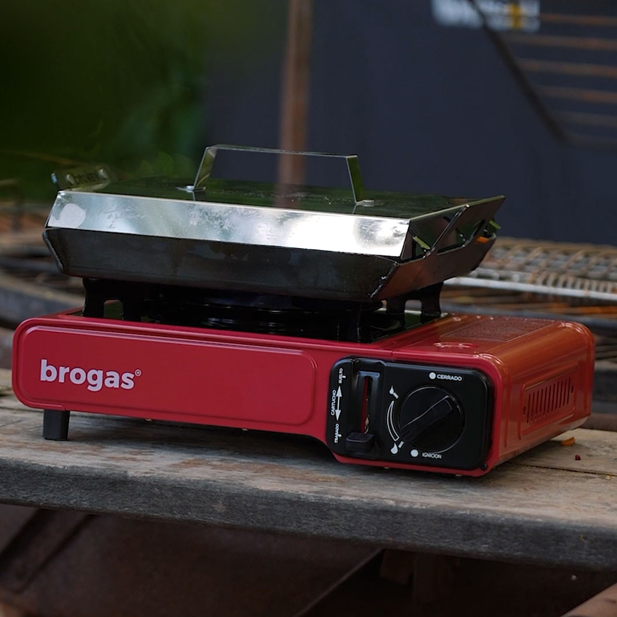 Anafe portátil de camping Brogas rojo con una plancha encima, al aire libre
