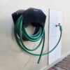 Soporte para manguera instalado en la pared junto a una canilla, con la manguera enrollada