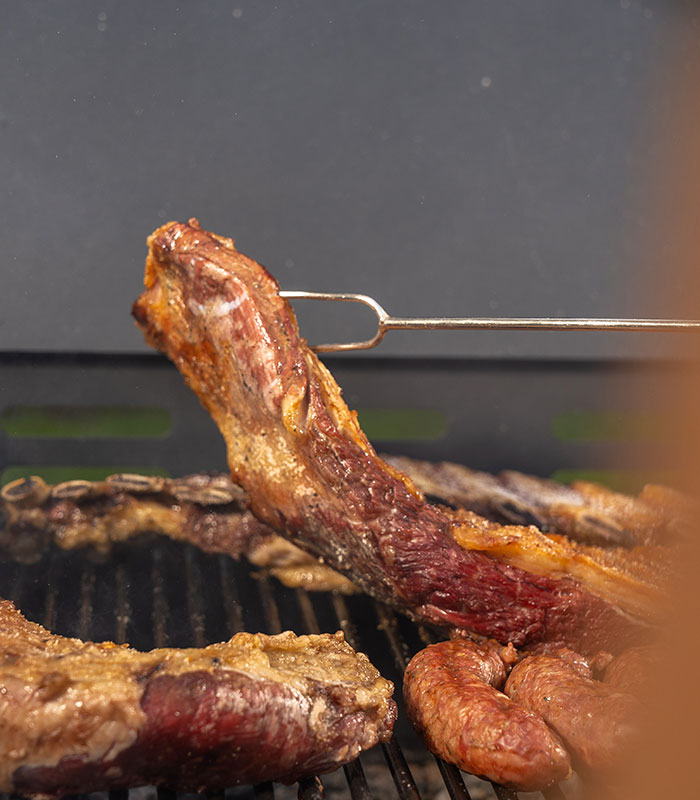 6113-CONTEXTO.jpg Tenedor parrillero sosteniendo un corte de carne sobre la parrilla