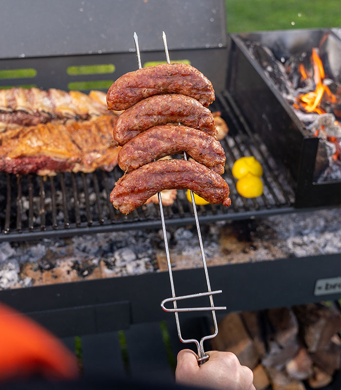 6121-CONTEXTO.jpg Pinche parrillero sosteniendo chorizos sobre la parrilla